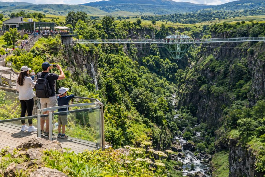 Visitors overlooking Dashbashi Canyon and Diamond Glass Bridge surrounded by green mountains in Georgia